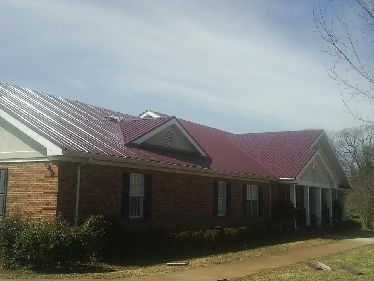Red metal roof with gabled entries on a long brick building, from a Hail Damage Roof Repair job in Murrayville