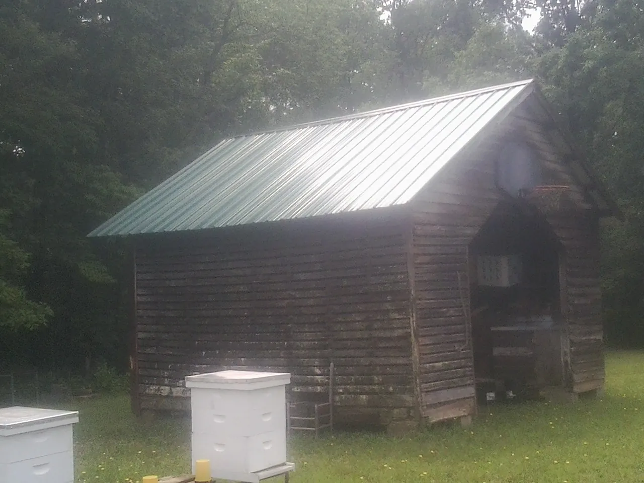 Green metal roof on a weathered barn beside stacked beehives in Murrayville