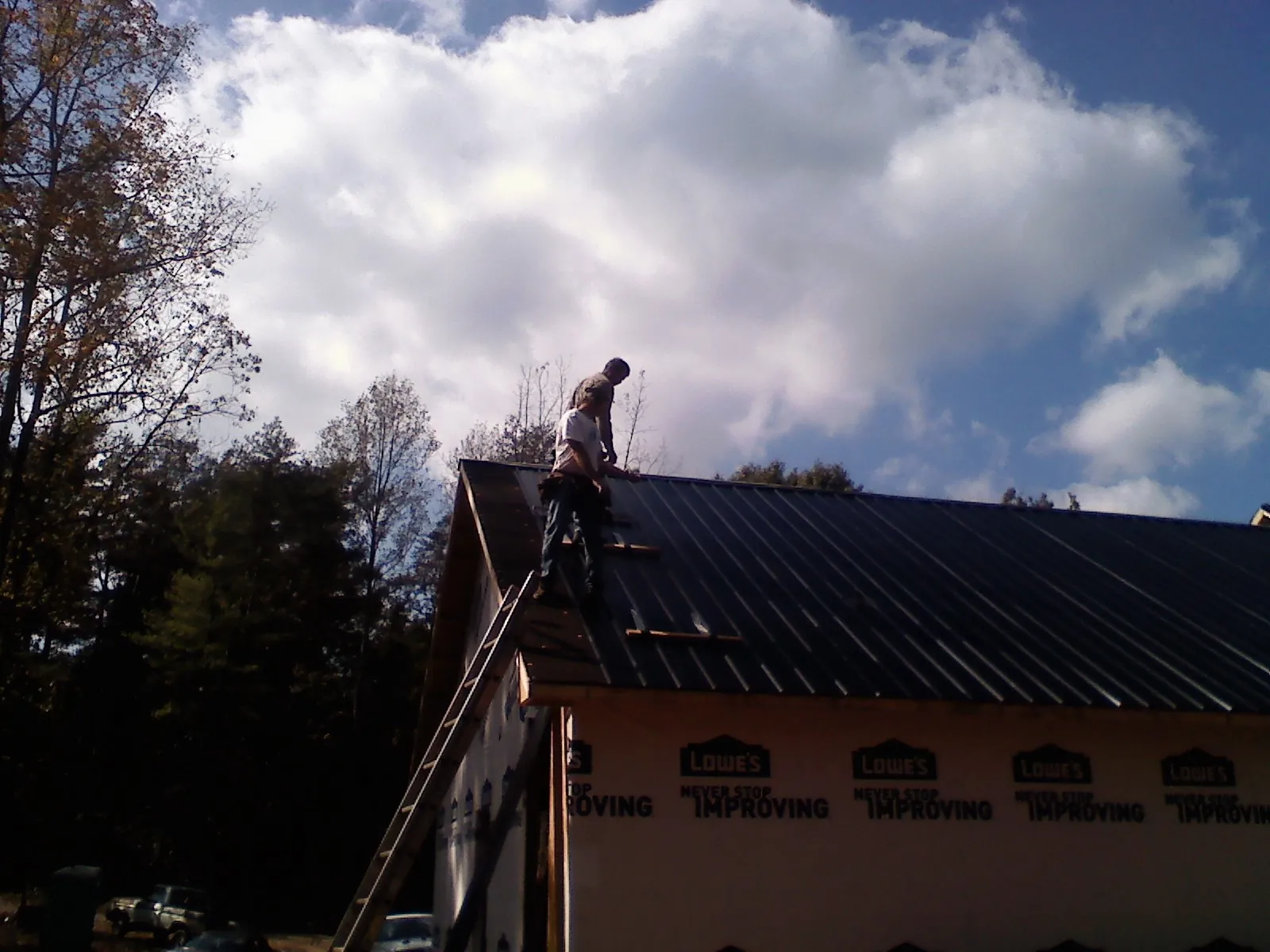 Roofer fastening dark metal panels high against a cloudy sky, from a Roof Inspection job in Murrayville