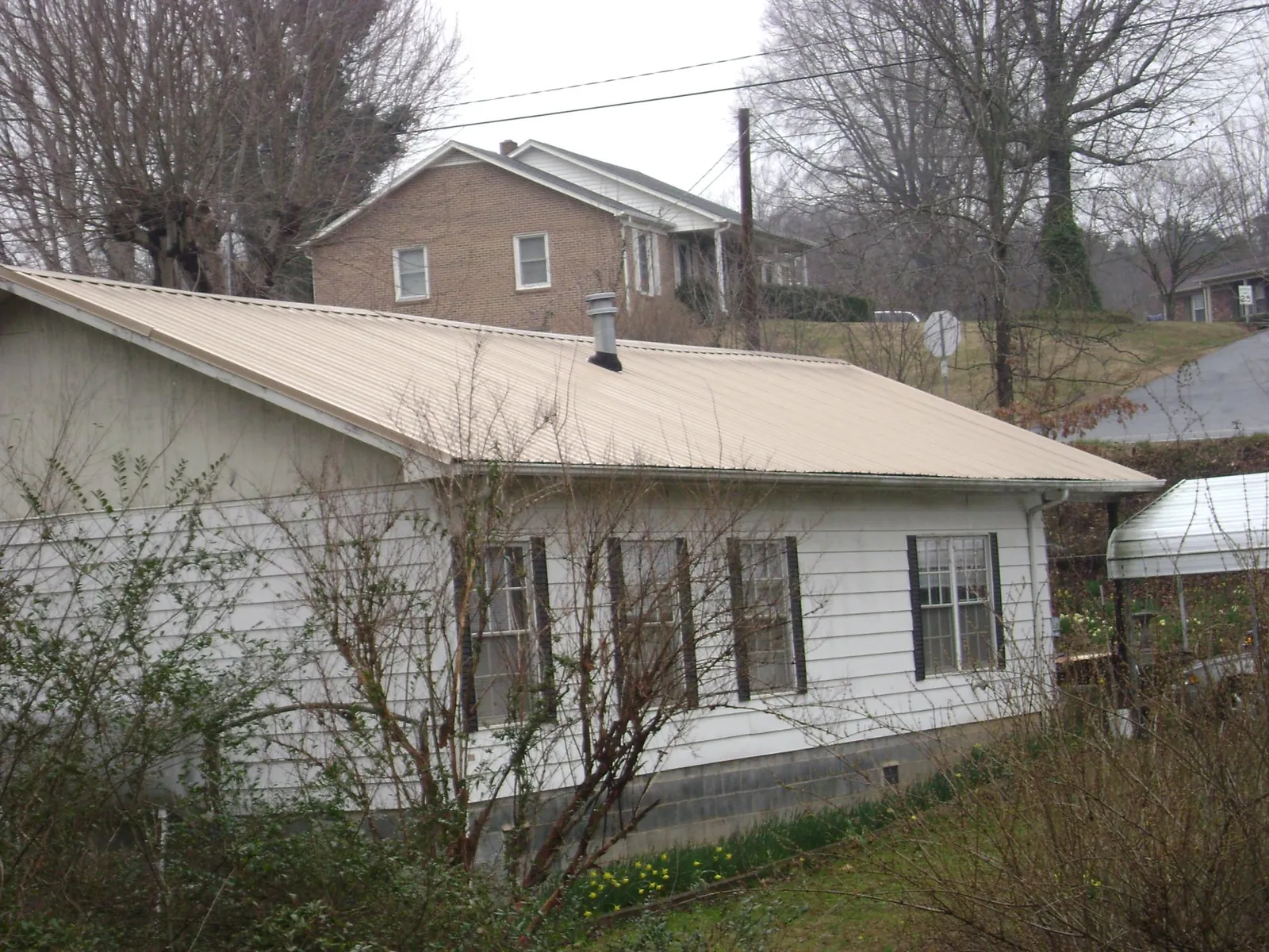 Tan metal roof on a white sided house set into a hillside — Commercial Roofing by Roofing Brothers in Murrayville